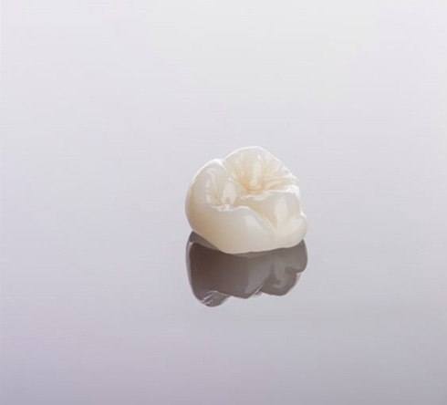Ceramic dental crown isolated on reflective surface