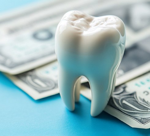 Large model tooth next to dollar bills on light blue surface